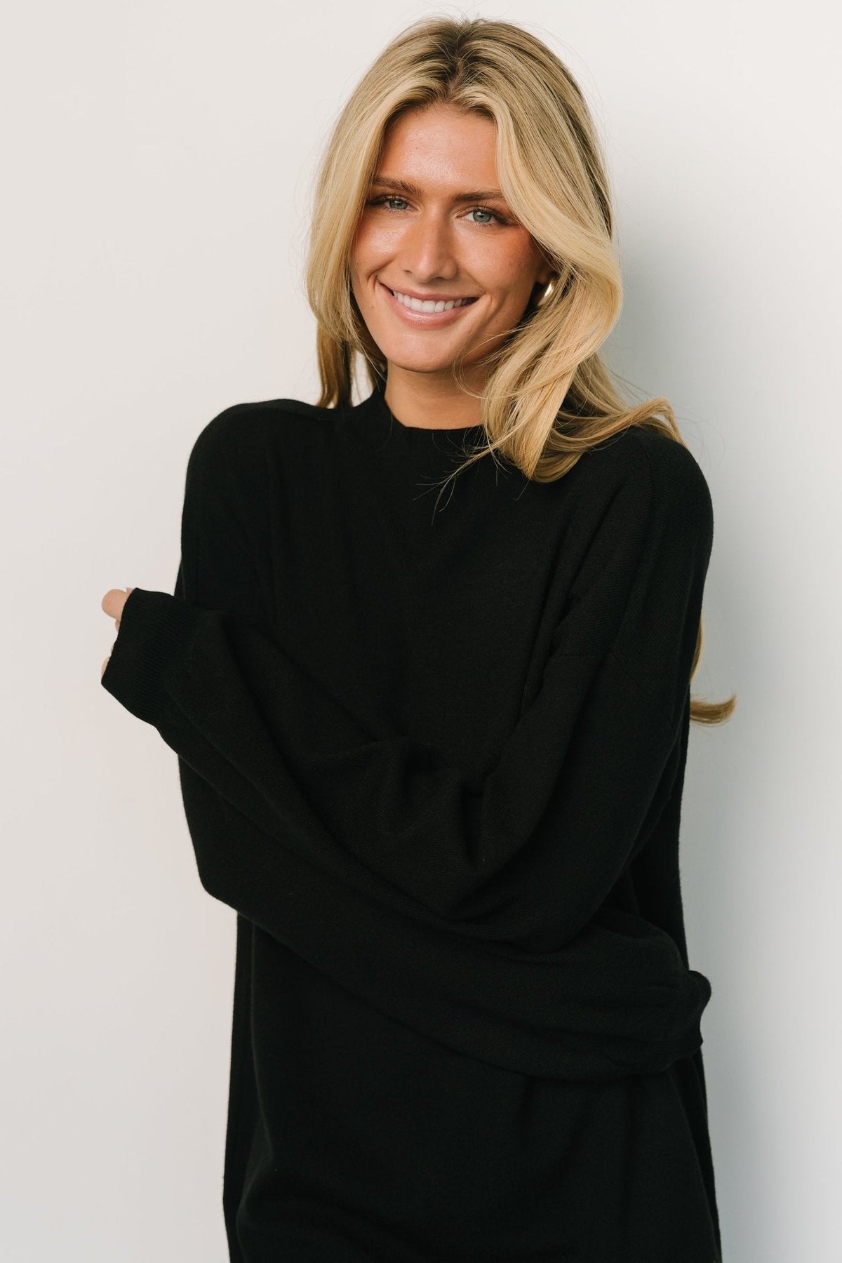 Studio shot of the black mock-neck sweater dress on a mannequin, showing overall shape, sleeve volume, and short length for styling reference.
